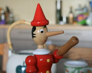Wooden Pinocchio on the table. Pinocchio is known for having a long nose that becomes longer when he is under stress, especially while telling a lie.