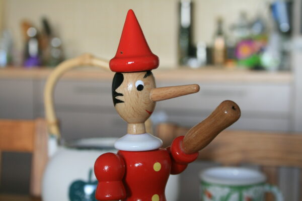 Wooden Pinocchio on the table. Pinocchio is known for having a long nose that becomes longer when he is under stress, especially while telling a lie.