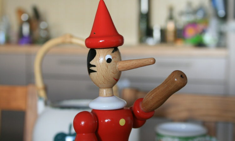 Wooden Pinocchio on the table. Pinocchio is known for having a long nose that becomes longer when he is under stress, especially while telling a lie.